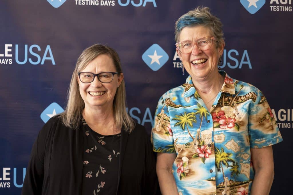 Lisa and Janet standing in front of a blue Agile Testing Days USA event backdrop.